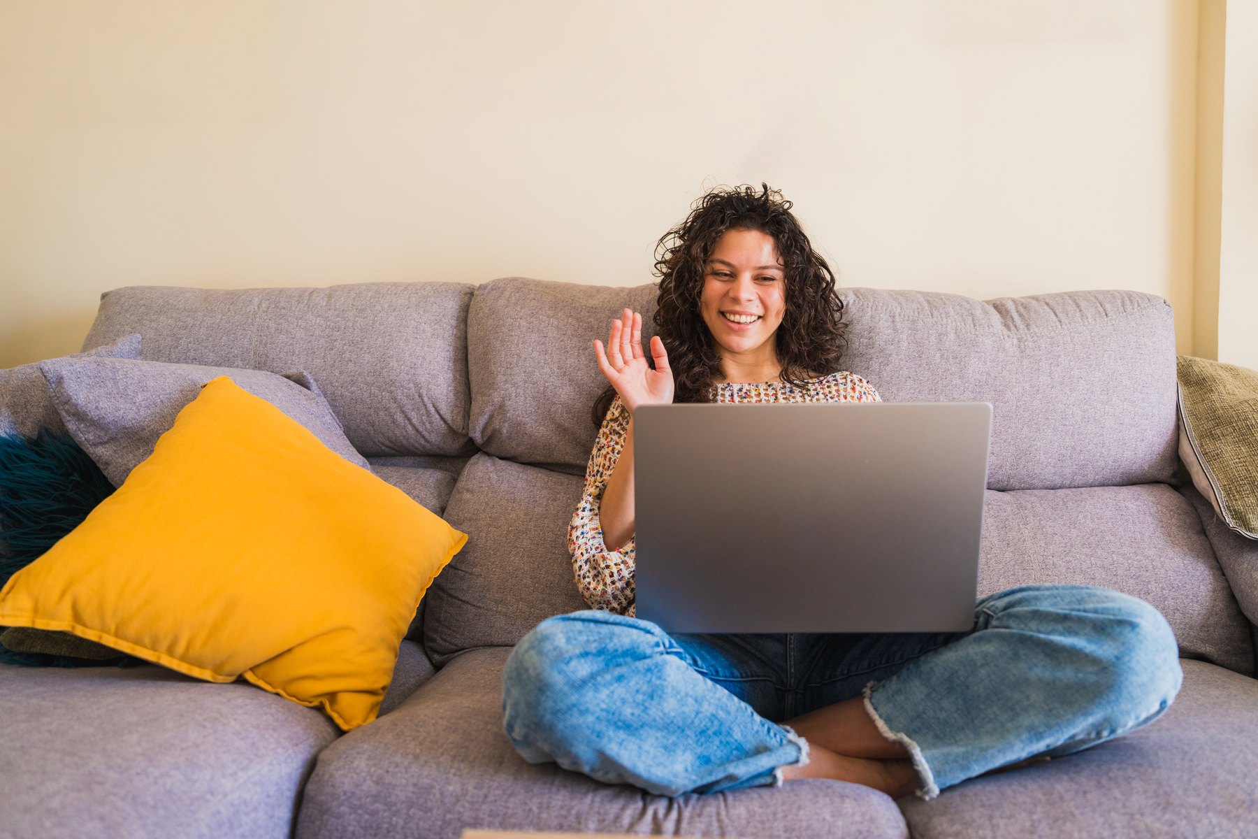 Cheerful woman waving during a video call from a sofa